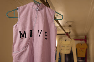 Three garments are hung on a pipe in the middle of a long hallway. The shirt in the foreground reads MOVE. 