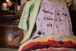 Stack of garments inside an apartment; one is a flowered, button-down tank top that reads, 