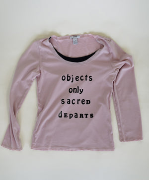 Long sleeved, pink shirt. In black lettering the garment reads, "Objects only sacred departs."