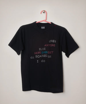 Pink, blue, and white sequined letters adorn the front of a black T-shirt. It reads, "Does anyone else here ever get as scared as I do."