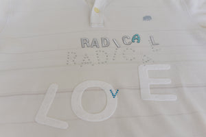 On the front of a white polo, felt, embroidered, and sequined iron-on letters spell out the message, "Radical love."